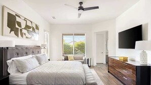 Ein modernes Schlafzimmer mit einem großen Bett, einem Schminktisch, einem Fernseher und einem Deckenventilator.