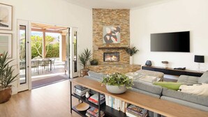 Ein modernes Wohnzimmer mit einer Wand aus Stein, einem Flachbildfernseher, einer Couch und einem Couchtisch mit Büchern und einer Pflanze.