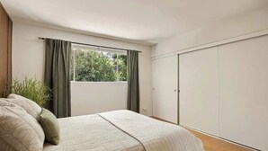 A bedroom with a bed, a window with curtains, a wardrobe, and a plant. - Hugh Kaptur Hideaway Villa (Palm Desert)