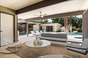 An outdoor seating area with a pool, lounge chairs, and a ceiling fan. - Hugh Kaptur Hideaway Villa (Palm Desert)