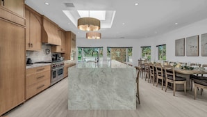 A modern kitchen with wooden cabinets, a marble island, and a dining area with a large table and chairs. - Luxury 6br Palm Springs Retreat With Private Pool Spa (Palm Springs)