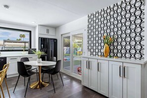 A modern kitchen with white cabinets, a dining area with black chairs, and a patterned wall. - Private Palm Springs Oasis With Saltwater Pool Spa (Palm Springs)