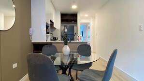 A modern dining area with a glass table and four chairs, a kitchen in the background, and a round mirror on the wall. - w Modern Cozy 2BR in the Heart of San Isidro (Lima)