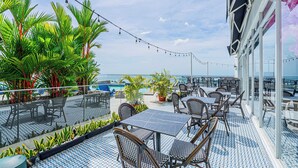 A rooftop bar with outdoor seating, palm trees, and a view of the ocean. - w Amazing Comfy 1BR w Pool on Avenida Balboa (Panama City)