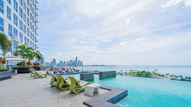A rooftop pool area with lounge chairs, a small table, and a view of the city skyline and ocean. - w Amazing Comfy 1BR w Pool on Avenida Balboa (Panama City)