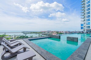A swimming pool with lounge chairs, a view of the ocean, and a distant pier. - w Amazing Comfy 1BR w Pool on Avenida Balboa (Panama City)