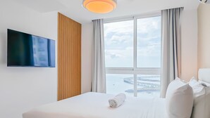 A hotel room with a bed, a TV, a large window with a view, and a ceiling light. - w Amazing Comfy 1BR w Pool on Avenida Balboa (Panama City)