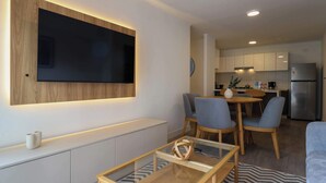 Ein modernes Wohnzimmer mit einem Flachbildfernseher, der an einer Holzvertäfelung angebracht ist, einem Glastisch und einem Essbereich mit Stühlen.