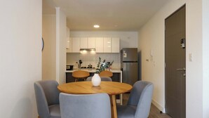 Eine moderne Küche mit weißen Schränken, einem Edelstahl-Kühlschrank und einem Essbereich mit zwei grauen Stühlen und einem Holztisch.