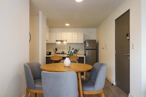 A modern kitchen with white cabinets, a stainless steel refrigerator, and a dining area with two grey chairs and a wooden table. - w Amazing Cozy 3BR w Balcony in Miraflores (Lima)