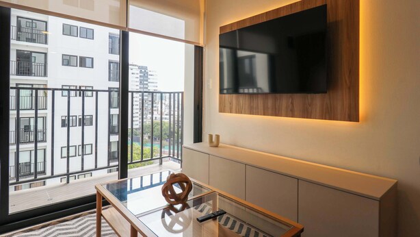 Ein modernes Wohnzimmer mit großem Fenster, einem an der Wand montierten Flachbildfernseher und einem Glastisch.
