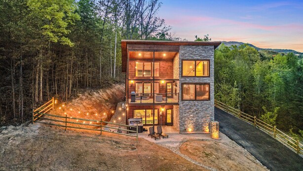 Een houten chalet met twee verdiepingen, een stenen gevel, een balkon en een patio met buitenmeubilair.