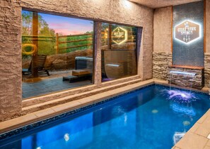 A pool with a stone wall and a window with a view of a wooden deck and a hanging tire. - Pool cabin, Theater, Sauna, Views, Firepit (Sevierville)