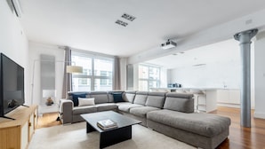 A modern living room with a sectional sofa, a coffee table, a TV, and a large window. - Spacious Modern Apartment in Central London (London)