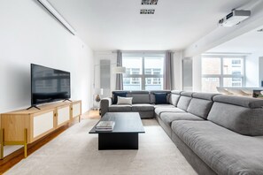 A modern living room with a flat-screen TV, a sectional sofa, a coffee table, and a large window providing natural light. - Spacious Modern Apartment in Central London (London)