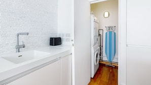 A modern kitchen with white countertops, a stainless steel faucet, a black toaster, and a white washing machine. - Spacious Modern Apartment in Central London (London)