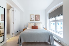 A bedroom with a large bed, two bedside tables, a window with blinds, and a door leading to another room. - Spacious Modern Apartment in Central London (London)