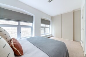 A bedroom with a bed, two windows with blinds, a wardrobe, and a radiator. - Spacious Modern Apartment in Central London (London)
