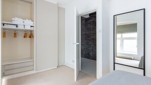 A modern bedroom with a bed, a wardrobe with folded clothes, a dark textured wall, and a large mirror. - Spacious Modern Apartment in Central London (London)