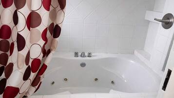 Un baño con una bañera blanca, una cortina de ducha con un diseño circular y paredes de azulejos blancos.