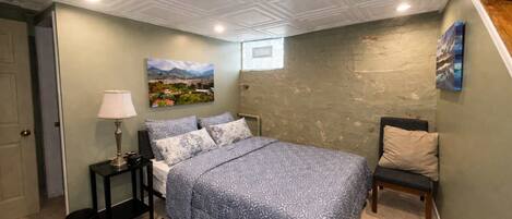 A bedroom with a bed, a nightstand, a lamp, a chair, and a painting on the wall.
