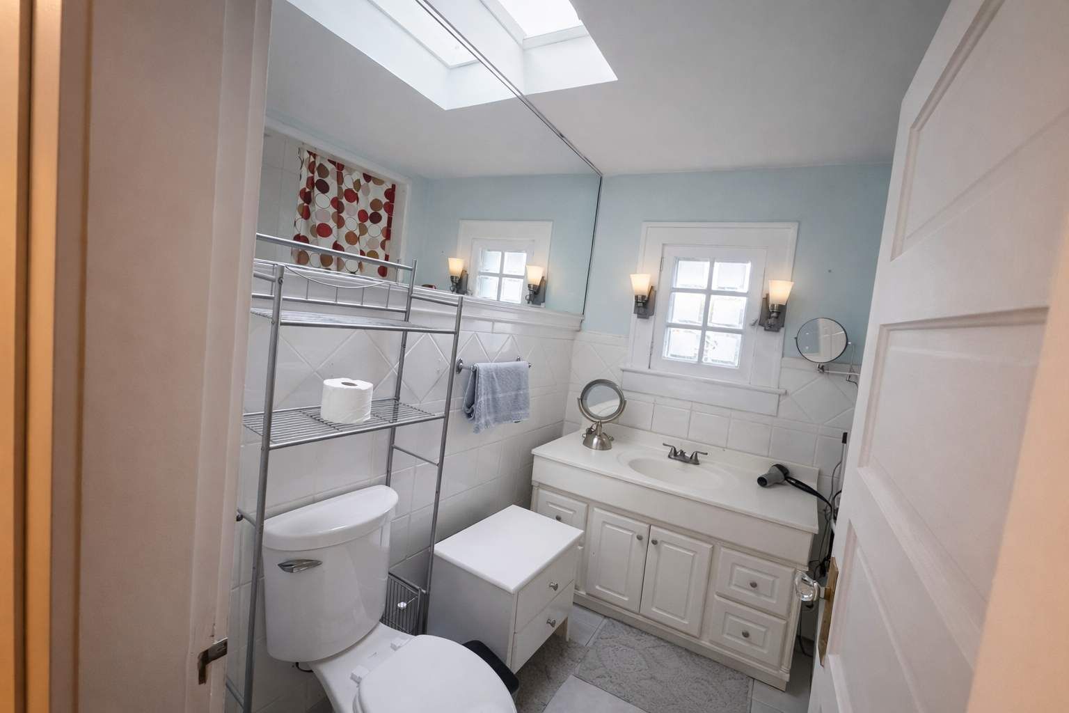 A bathroom with a skylight, toilet, sink, and vanity with a mirror.