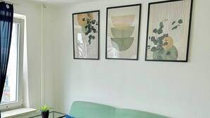 En grøn sofa med blå puder, et glasbord og tre abstrakte billeder på væggen.