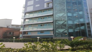 Un edificio de varios pisos con fachada de vidrio, balcones y un patio con plantas.