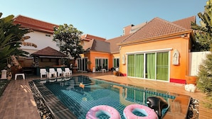 Piscina con lettini e cerchi gonfiabili, circondata da una terrazza con pavimento piastrellato e piante in vaso.