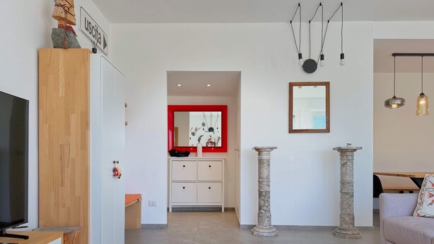 A modern living room with a TV, wooden cabinet, white furniture, a red-framed mirror, stone columns, and a fur rug. - The Clover Close to Citylife Metro and Fiera (Milan)