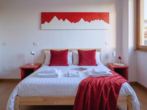 Ein ordentlich bezogenes Bett mit weißen Leinentüchern, roten Kissen und einer roten Dekoration darüber.