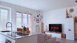 A modern kitchen with a central island, a dining area with a sofa, and a TV displaying 'NETFLIX' on the wall. - The Clover Close to Citylife Metro and Fiera (Milan)
