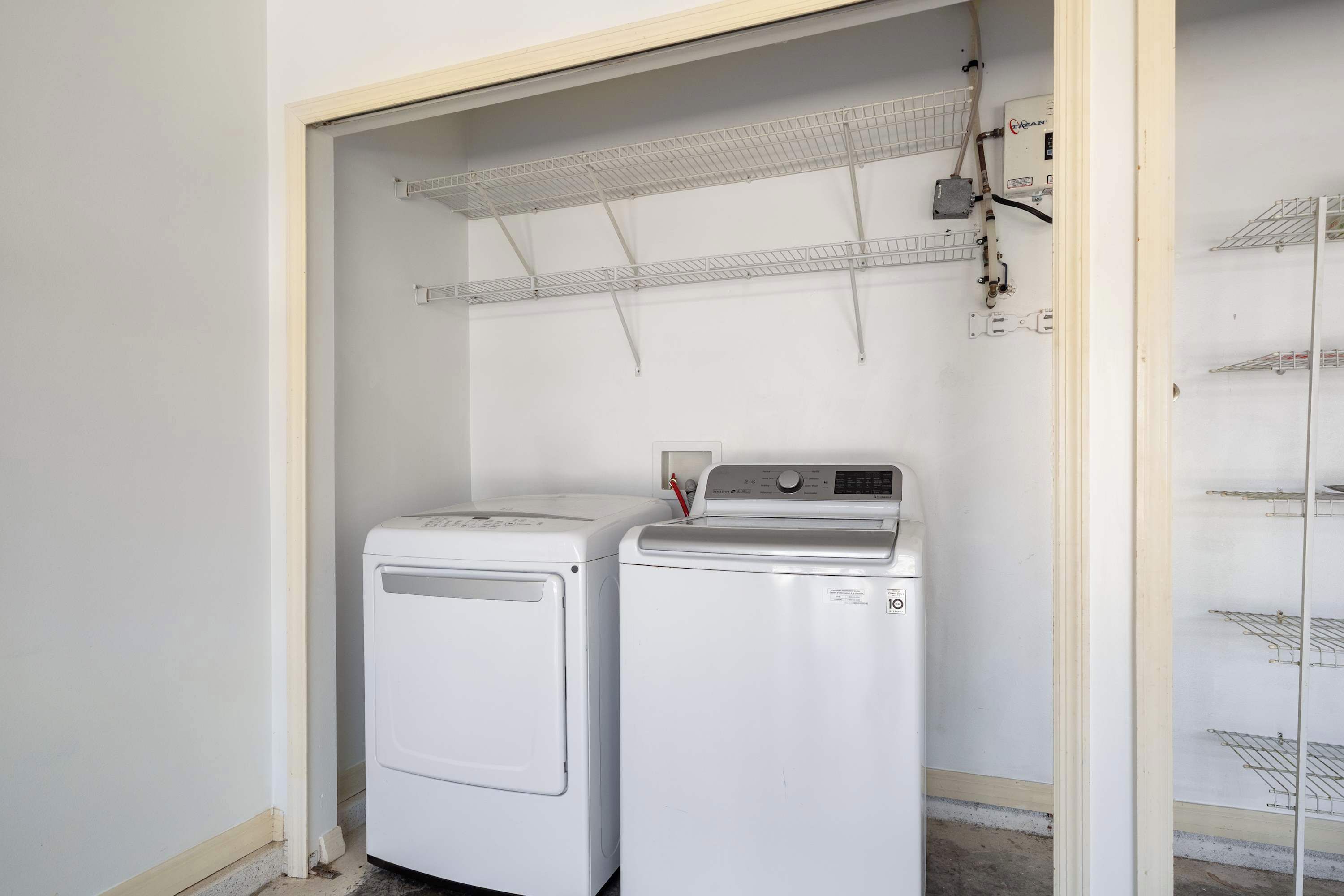 Un espace buanderie comprenant deux sèche-linge blancs, une étagère en métal et une prise de courant.