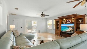 A living room with a leather sofa, a TV, and a ceiling fan. - Spacious 5BR Pool Oasis Near Disney Resort (Sebastian)