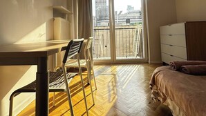 Habitación de hotel con cama, escritorio con silla, cómoda y puerta corrediza de vidrio que da a un balcón.