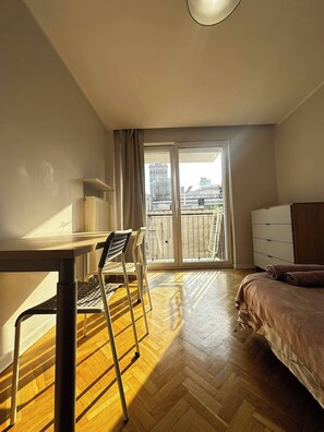 A hotel room with a bed, a desk with a chair, a dresser, and a sliding glass door leading to a balcony. - Golden Escape 3 Rooms Apart (Warsaw)