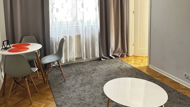 Una sala de estar moderna con comedor, cortinas grises, una lámpara de techo y piso de madera en espiga.