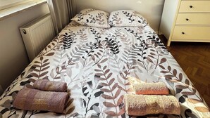 Un dormitorio con cama, radiador, ventana con cortinas, mesita de noche y cómoda.