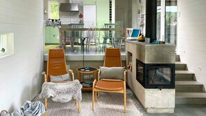 Una sala de estar acogedora con chimenea, un comedor con sillas, y una cocina visible a través de una puerta abierta.