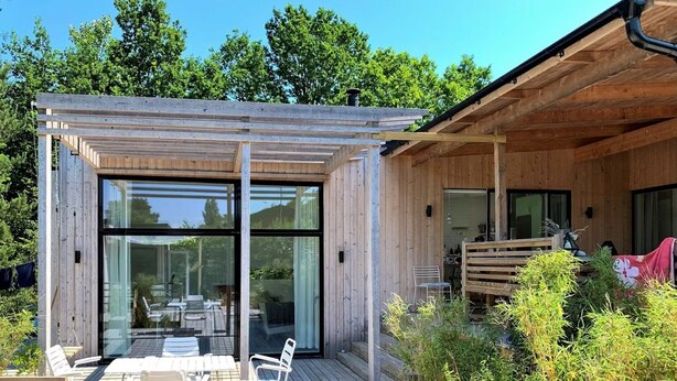 Una terraza de madera con mobiliario exterior y cerramiento de vidrio.