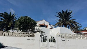 Un edificio bianco con tetto rosso, palme e un cancello con un cartello numerico.