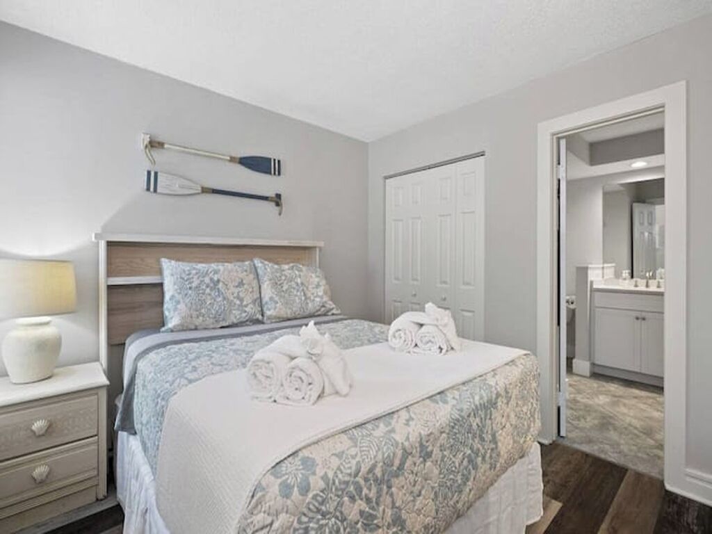 Une chambre à coucher comprenant un lit, une table de chevet, une lampe, une porte et une vue sur la salle de bain.