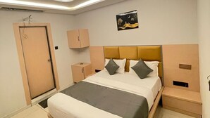 A modern bedroom with a bed, nightstands, a door, and a ceiling light fixture. - HOTEL HILLS (Ahmedabad)