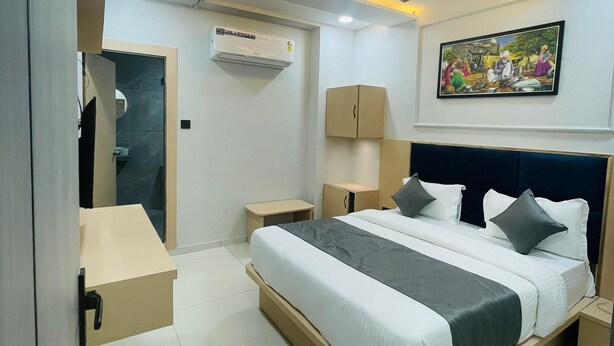 A modern hotel room with a bed, bedside tables, an air conditioning unit, a ceiling fan, and a painting on the wall. - HOTEL HILLS (Ahmedabad)
