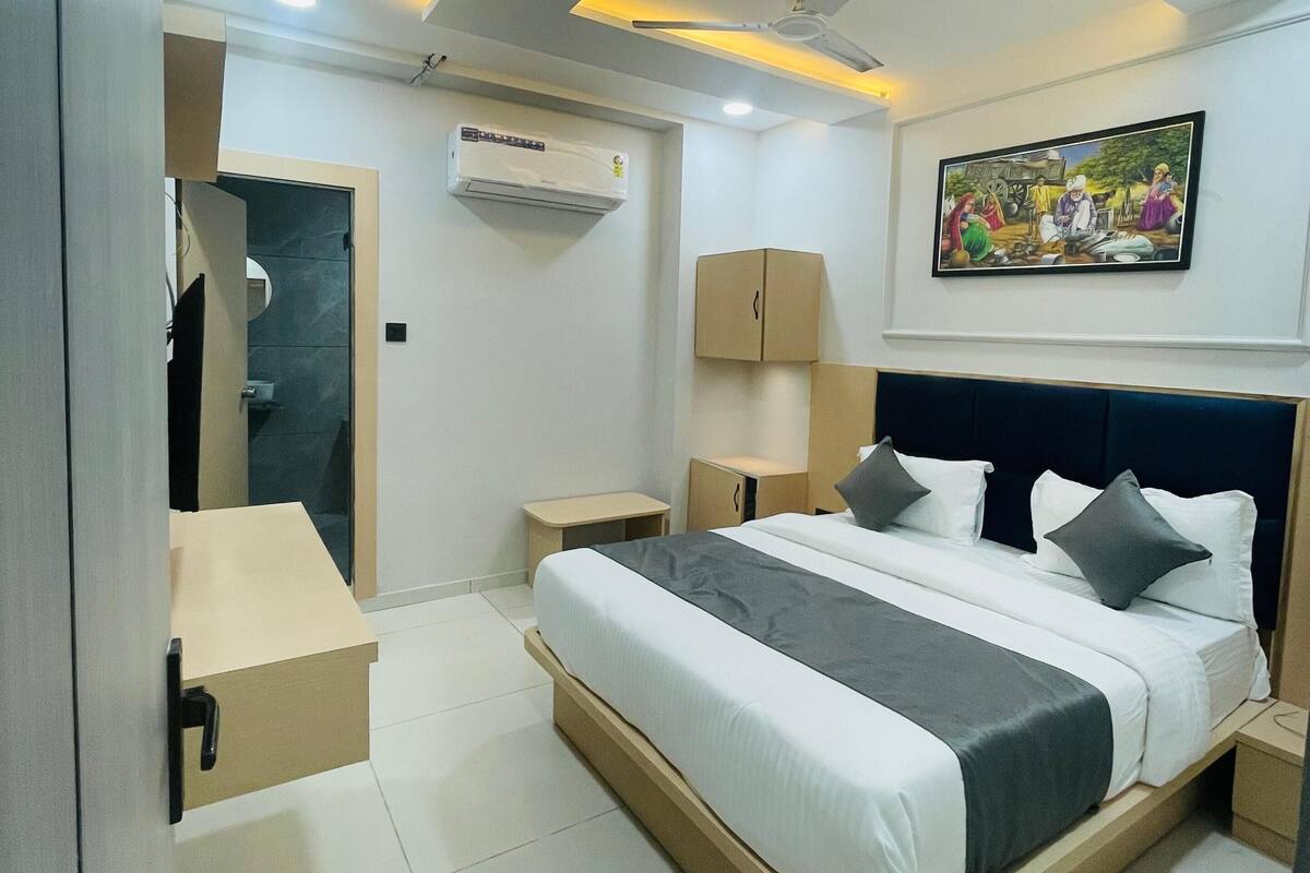 A modern hotel room with a bed, bedside tables, an air conditioning unit, a ceiling fan, and a painting on the wall.