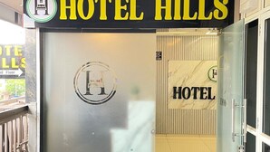 A hotel entrance with a glass door, a logo above the name, and a small green mat at the entrance. - HOTEL HILLS (Ahmedabad)