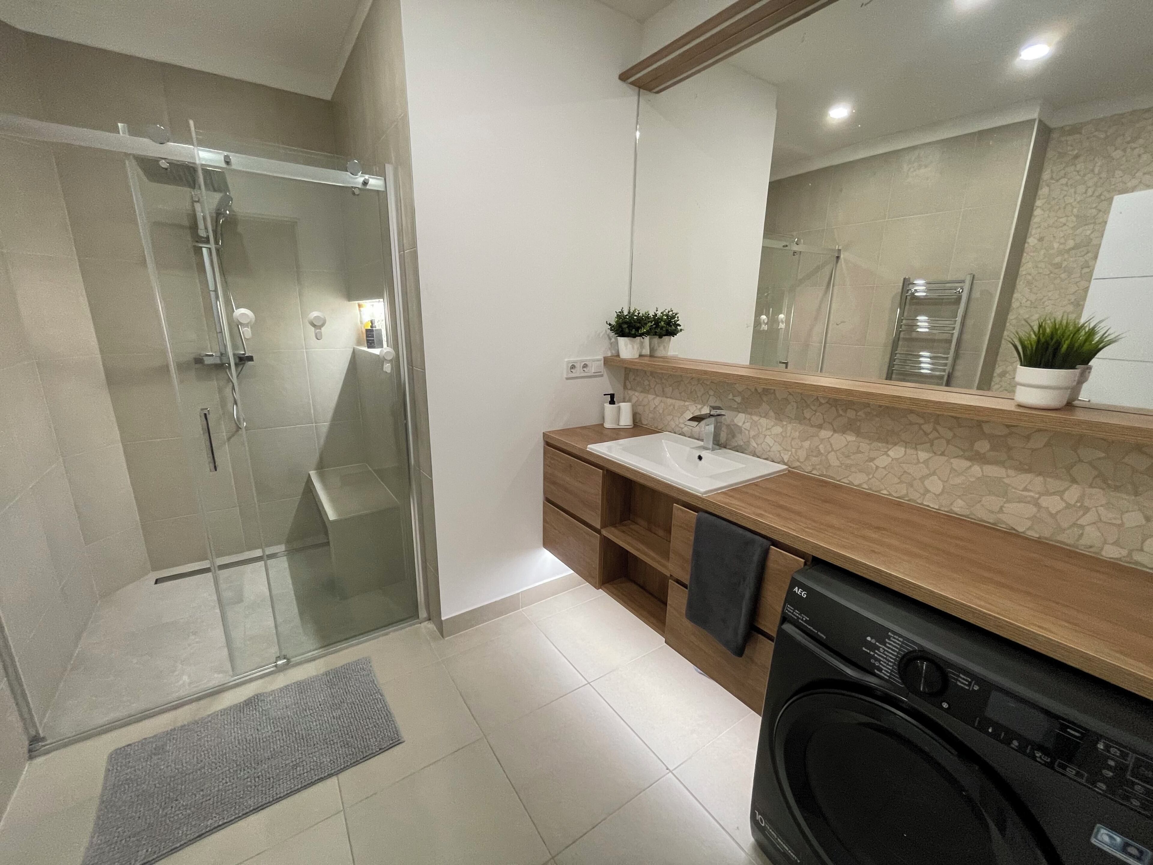 Une salle de bain moderne avec une douche à parois de verre, un meuble-lavabo en bois avec un évier, un miroir et un lave-linge.