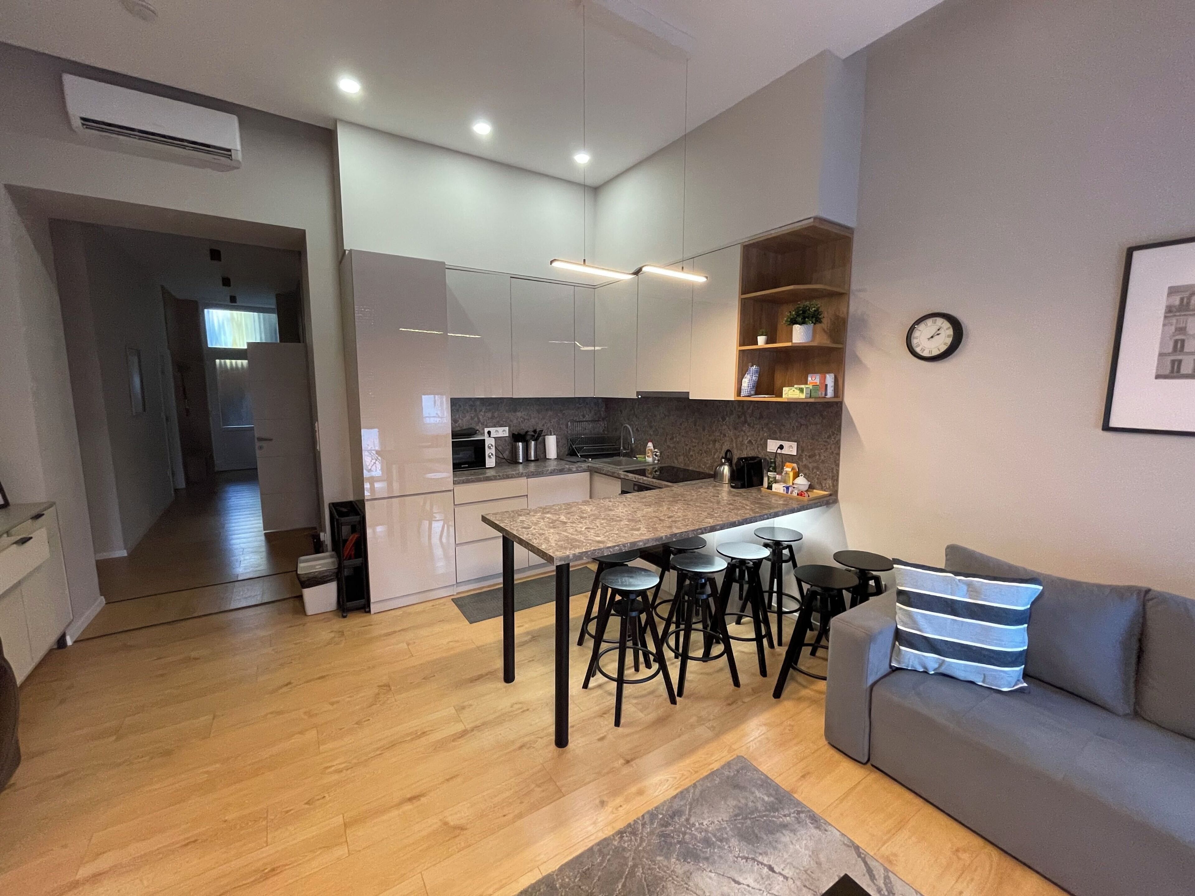 Une cuisine moderne avec un îlot central, des tabourets de bar, un canapé et une horloge au mur.