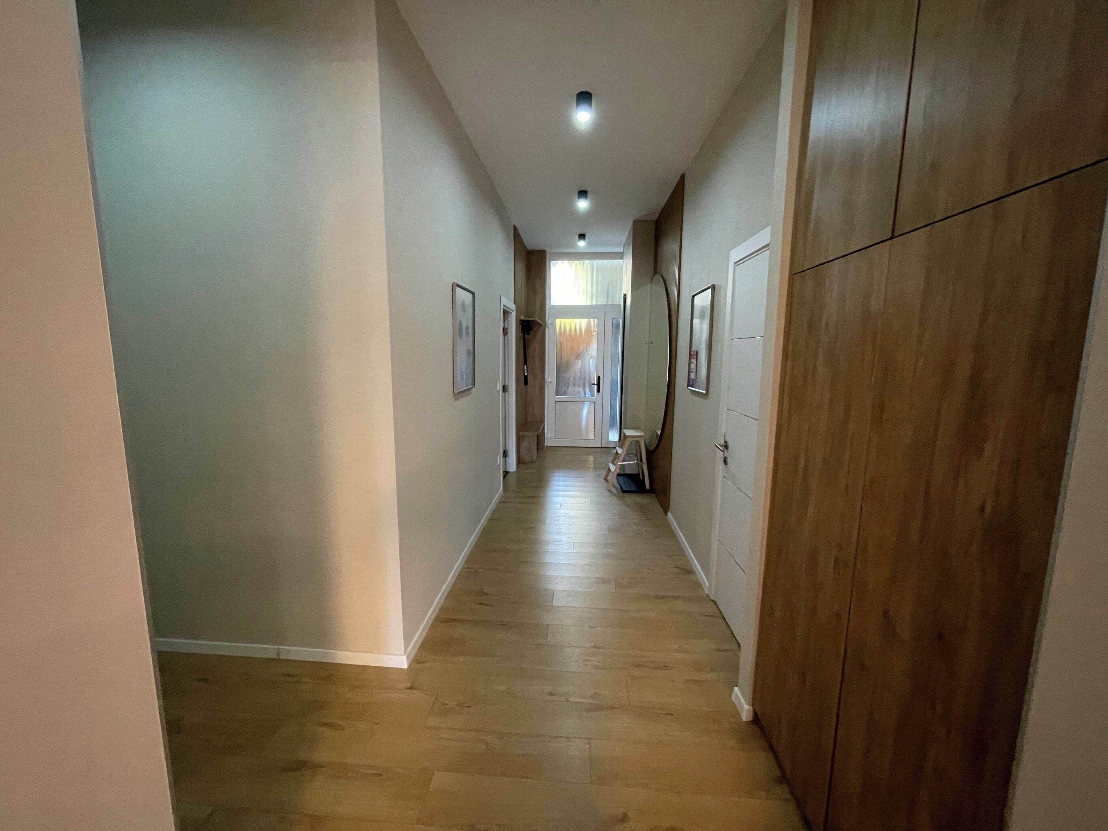 Un couloir doté d’un plancher en bois, de murs blancs et de portes donnant accès aux pièces.