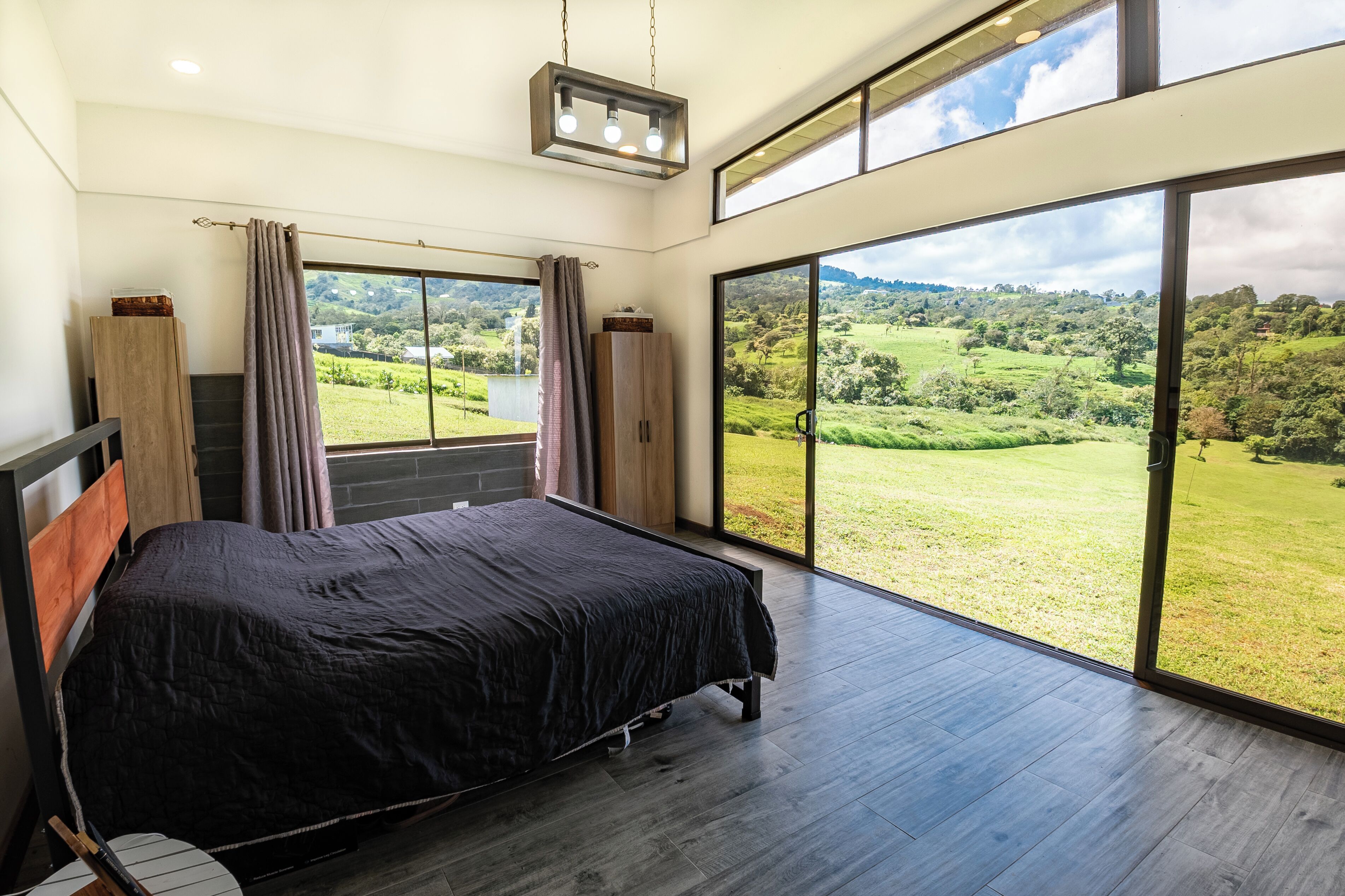 A bedroom with a large bed, a view of a green landscape, and a sliding glass door.